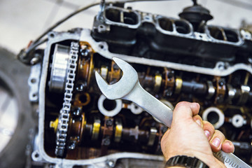 hand holds a wrench on the background of the engine being repaired