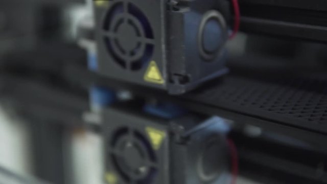 Close up view to a FDM 3D Printer extruder while working on mirror glass with black PLA filament. Shallow depth of field.