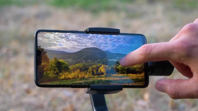 Man Retouching A Landscape Picture On His Smartphone On A Gimbal in slowmotion notch smartphone no brand