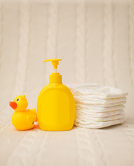 Close up baby hygiene items. stack of diapers, liquid soap and yellow duck on beige plaid in selective focus