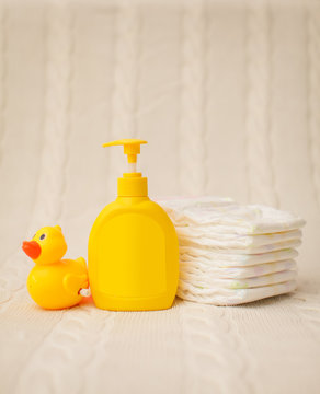 Close Up Baby Hygiene Items. Stack Of Diapers, Liquid Soap And Yellow Duck On Beige Plaid In Selective Focus