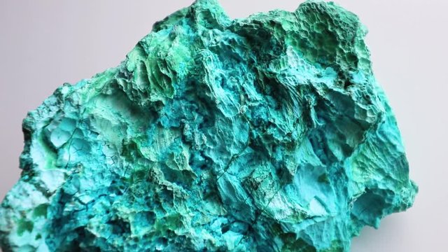 Downwards panning, top view of a beautiful blue and green mineral called Chrysocolla, against a white background.