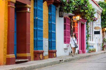Fototapeta premium Beautiful woman on white dress walking alone at the colorful streets of the colonial walled city of Cartagena de Indias