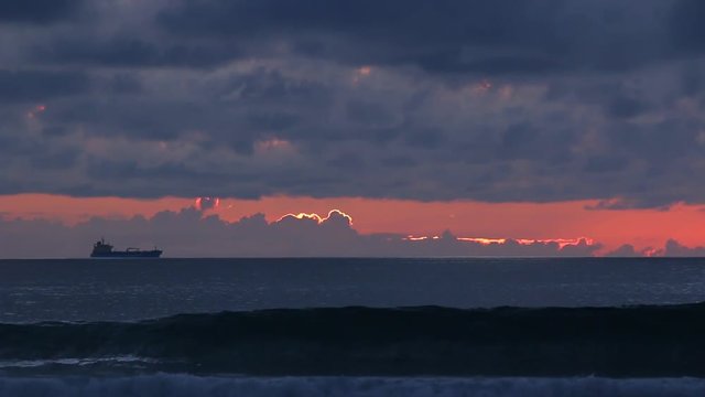 Lone surfer watches ship out to sea at twilight, WIDE.