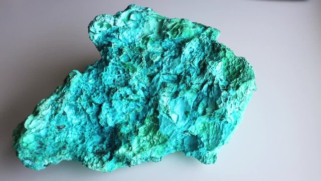 Panning left to right, top view of a beautiful blue & green mineral called Chrysocolla, against a white background.