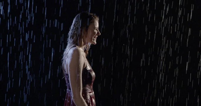Attractive young woman with blonde hair gets soaking wet as she walks through rain at night. Mid shot, slow motion 4K recorded at 60fps