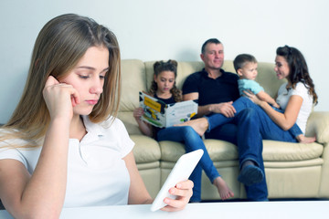 teenage girl looks in the phone alone on the background of communicating family