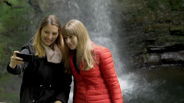 Two girls take selfies in front of a waterfall in Ireland - travel photography