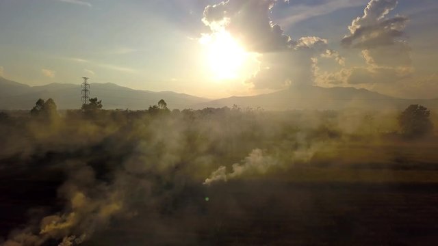 Aerial view. The morning sunrises with dusty smoke from dry grass is burning on the field. Burning old chaff on the farmland.