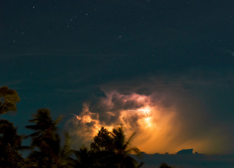 Dramatic night thunderstorm in the starry sky above the trees and sea