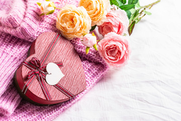 Beautiful gift box with a knitted sweater and a rose on a white fabric background 