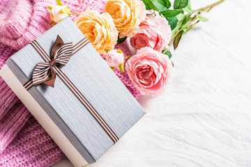 Beautiful gift box with a knitted sweater and a rose on a white fabric background 