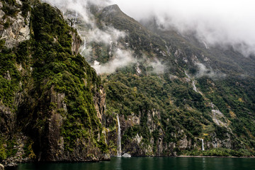 Milford Sound, boat beneath the waterfall in the mist and clouds