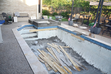 Empty swimming pool under remodel with new tile and coping with wooden debris 