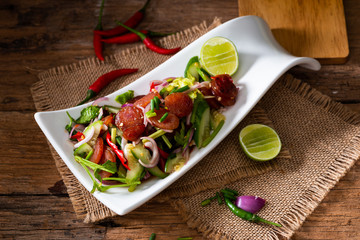 Spicy Chinese pork sausage with vegetable Thai salad in white plate on wood background