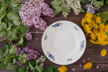 Fototapeta na wymiar Plate and decor of flowers on the background of vintage wooden planks. Vintage background with flowers of dandelion and lilac and a place under the text. Flat lay. Cutlery. Vintage.