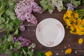 Plate and decor of flowers on the background of vintage wooden planks. Vintage background with flowers of dandelion and lilac and a place under the text. Flat lay. Cutlery. Vintage.