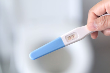 Obraz premium Closeup woman hand holding pregnancy test in bathroom, health care concept, selective focus
