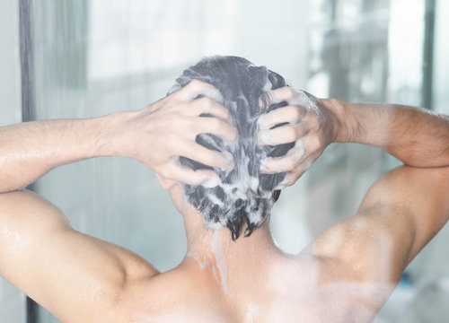 Closeup young man washing hair with with shampoo in the bathroom, vintage tone, selective focus