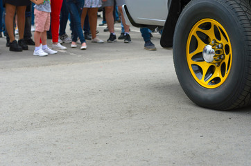 Rear Wheel of a SUV Truck with Yellow Spokes and Shiny Center Cap, Visitors at a Car Show or Event.