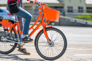 Woman on an orange bike with basket waits at crossroads allowing traffic light