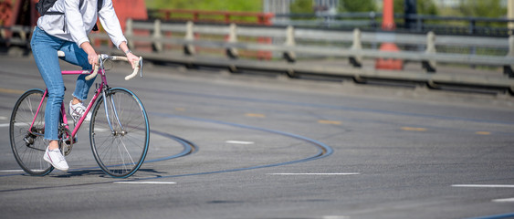 Young gentle girl cyclist in jeans and sneakers crosses the road by bike while driving through...