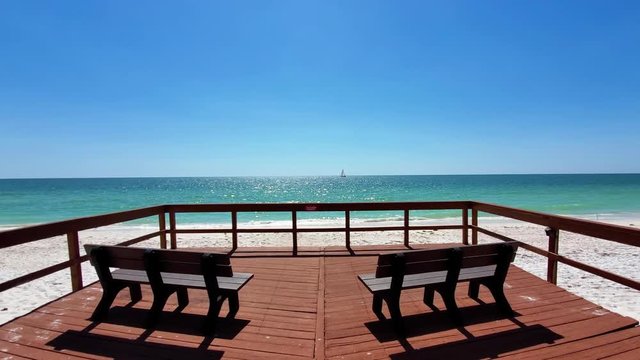Two wooden benches on a deck facing the beautiful ocean, with waves crashing and a boat moving in the horizon. Clearwater, Florida, USA. (FYI: footage available from a different angle in my portfolio)