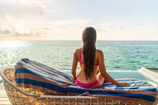 Sexy Bikini Woman From Behind Sitting Back On Lounger Chair At Luxury Resort Sun Tanning At Sunset By The Hotel Pool. Long Wet Brown Hair Brunette Model.