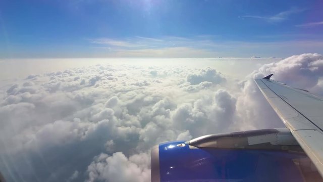 An amazing view of white clouds extending to the horizon, shot through the window of an airplane with sun rays shining from the top.