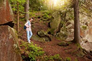 Naklejka na ściany i meble Slender serious female going down hill, being inspired by nature, wandering around stony slopes, forest trees, having vacation, following known path, wearing casual clothes. Travelling concept.