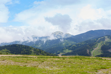 View of mountain with rocky foreground, green meadows, tourist path in distance, beautiful nature, amazing landscape, briliant scenery, green field on the bottom of mountains, blue sky with clouds.