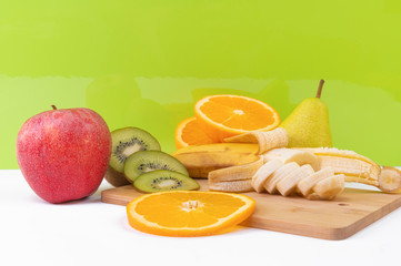 Sliced tropical fruits: kiwi, orange, banana on light wooden board.