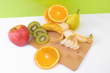 Sliced tropical fruits: kiwi, orange, banana on light wooden board.