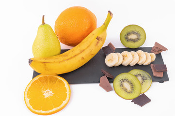 Top view of sliced kiwis and oranges, whole banana, chocolate on a bright background
