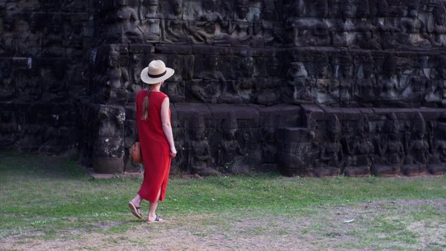Caucasian woman in red dress is exploring beautiful bas-reliefs of the Leper King terrace located in the northwest corner of the Royal Square of Angkor Thom, Cambodia