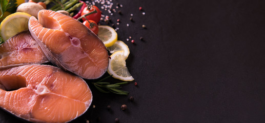 Fresh raw salmon fish steak with seasoning and vegetables on black stone background