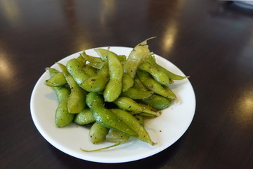 A plate of boiled green soybeans on table. A common side dish in Taiwanese restaurants. Also called vegetable soybean, edamame, or edamame bean. Food concept.