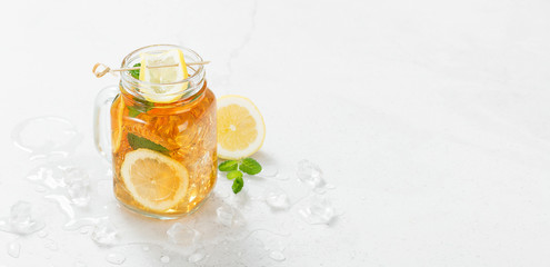 Iced tea with lemon slices and mint on light gray stone background.