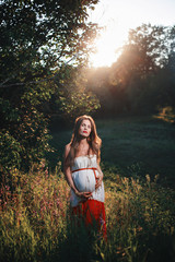 Young pregnant woman in the park outdoors. Calm pregnant woman in third trimester. Walking in...