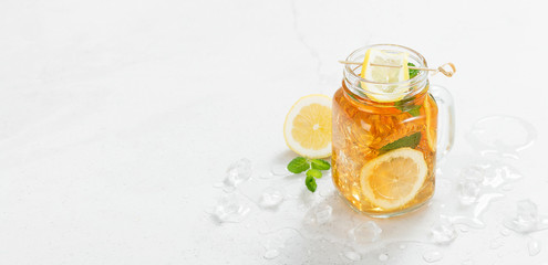 Iced tea with lemon slices and mint on light gray stone background.