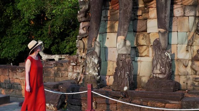 Woman in red dress is exploring elephants statues with big trunks at the Terrace of Elephants wall, part of the beautiful walled city of Angkor Thom, a ruined temple complex in Cambodia