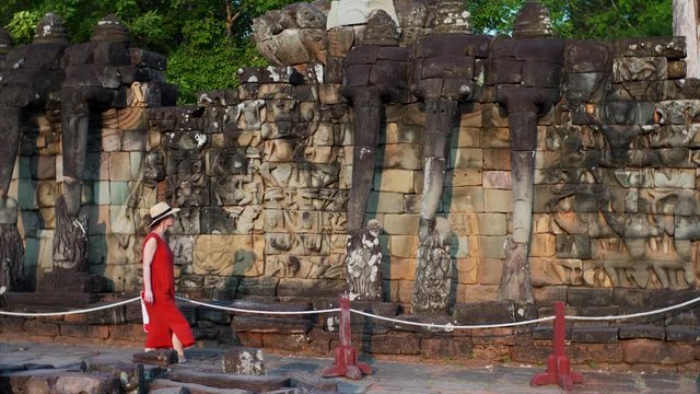 Woman tourist is exploring elephants statues with big trunks at the Terrace of Elephants wall, part of the beautiful walled city of Angkor Thom, a ruined temple complex in Cambodia