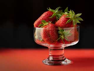 Strawberries in a glass vase on a red table and black background