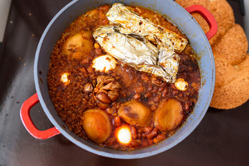 Hot plate for the Sabbath, a pot of spicy meat cooked with potatoes, barleys, wheat and eggs. Pot of cholent Hamin in hebrew, challah-special bread in Jewish cuisine. Traditional food Jewish Shabbat.