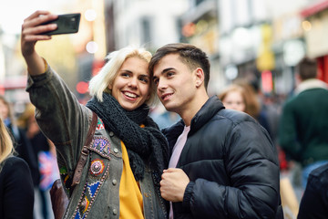 Happy couple of tourists taking selfie in a crowded street.