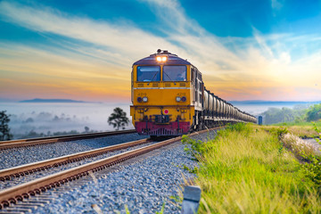 Yellow train on railway cross the mountain hill that covered by fog on sunrise. - obrazy, fototapety, plakaty