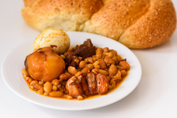 Close up Challah Shabbat bread and hamin or cholent in hebrew - Sabbath traditional food on white table in the kitchen.