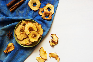 Obraz na płótnie Canvas Apple chips and cinnamon on white wooden table. Homemade dry dehydrated fruit slices, autumn fall snack, healthy vegetarian diet. Horizontal, top view, flatlay, copy space.