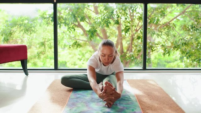 Girl doing yoga pose janu sirsasana in front of panoramic window with park view