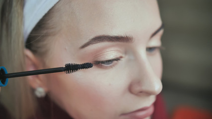 Beautiful blonde girl paints her eyelashes. Blonde girl.